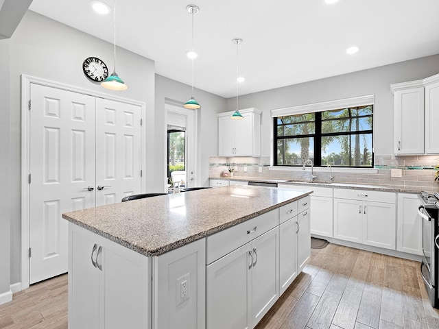 kitchen featuring light stone countertops, a kitchen island, white cabinets, and decorative light fixtures