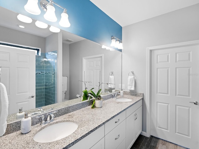 full bathroom featuring wood finished floors, tiled shower, a sink, and double vanity