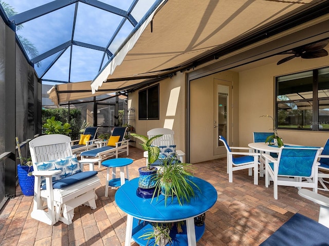 view of patio featuring glass enclosure, outdoor dining area, and a ceiling fan