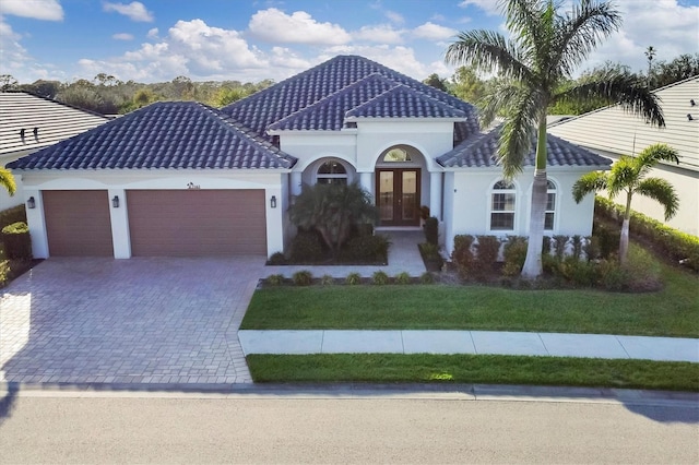 view of front of property with decorative driveway, a tile roof, an attached garage, and french doors