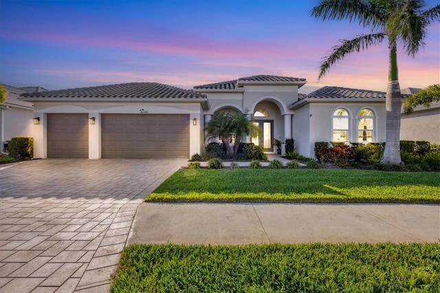 mediterranean / spanish home featuring a front lawn, a tiled roof, stucco siding, decorative driveway, and a garage