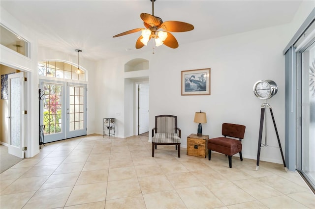 sitting room featuring light tile patterned floors, arched walkways, a ceiling fan, baseboards, and french doors