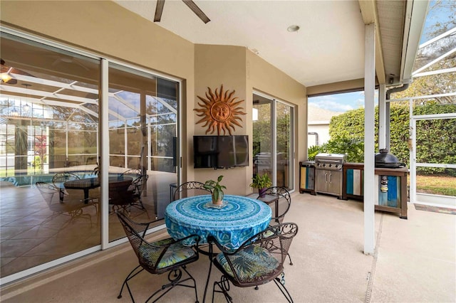 view of patio featuring a ceiling fan, glass enclosure, outdoor dining area, and grilling area