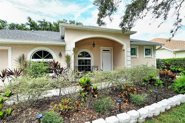 view of front of property featuring a garage, roof with shingles, and stucco siding