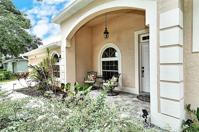 doorway to property with a porch, an attached garage, and stucco siding