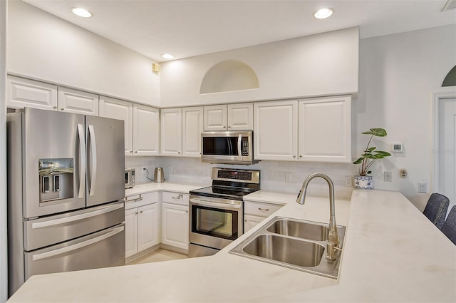 kitchen featuring stainless steel appliances, light countertops, backsplash, a sink, and a peninsula