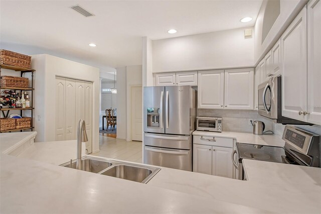 kitchen with a toaster, stainless steel appliances, light countertops, white cabinetry, and a sink