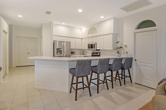 kitchen featuring a breakfast bar area, stainless steel appliances, a peninsula, visible vents, and white cabinets