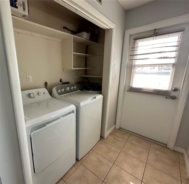 clothes washing area with washer and clothes dryer, light tile patterned flooring, and baseboards