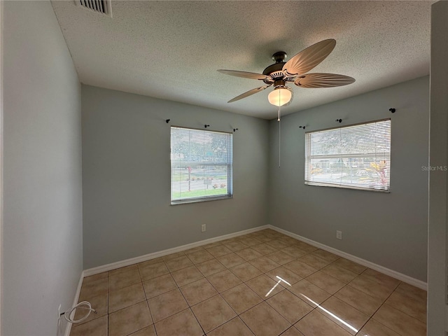 spare room featuring baseboards, ceiling fan, visible vents, and a textured ceiling