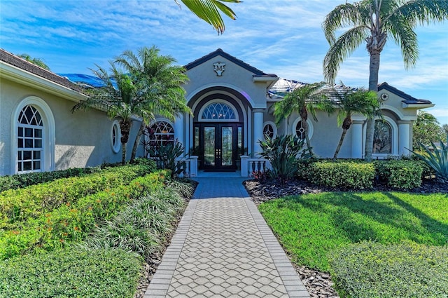 entrance to property with stucco siding, a lawn, and french doors