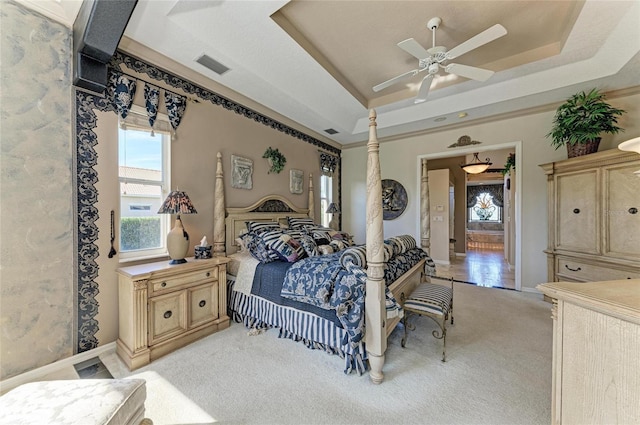 bedroom with light carpet, visible vents, a tray ceiling, and a ceiling fan