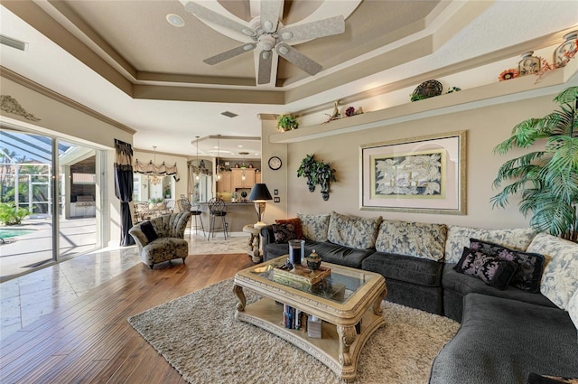 living room with visible vents, ceiling fan, ornamental molding, wood finished floors, and a tray ceiling