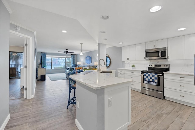 kitchen featuring a center island with sink, white cabinets, open floor plan, stainless steel appliances, and a sink