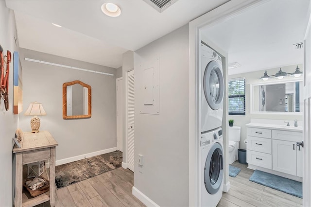 laundry room featuring laundry area, stacked washer / dryer, a sink, visible vents, and light wood finished floors