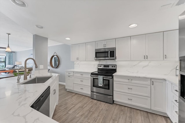 kitchen featuring appliances with stainless steel finishes, white cabinetry, hanging light fixtures, and a sink