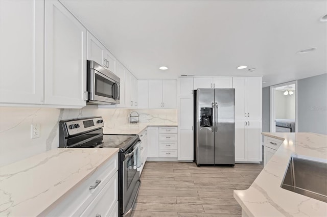 kitchen with light stone counters, decorative backsplash, appliances with stainless steel finishes, wood tiled floor, and white cabinetry