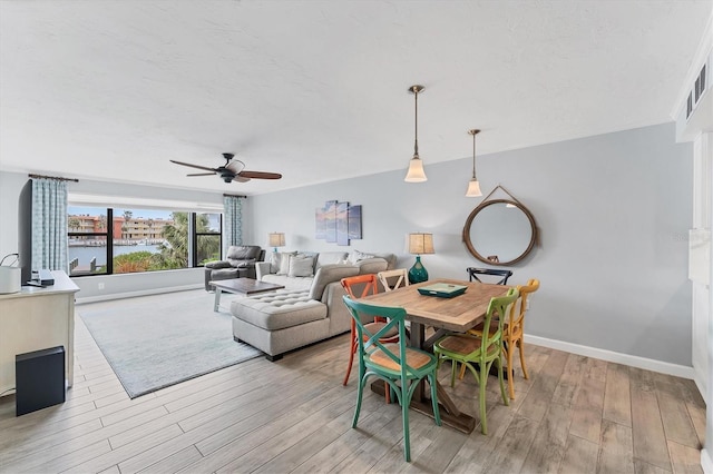 dining area featuring light wood-style flooring, a textured ceiling, baseboards, and a ceiling fan