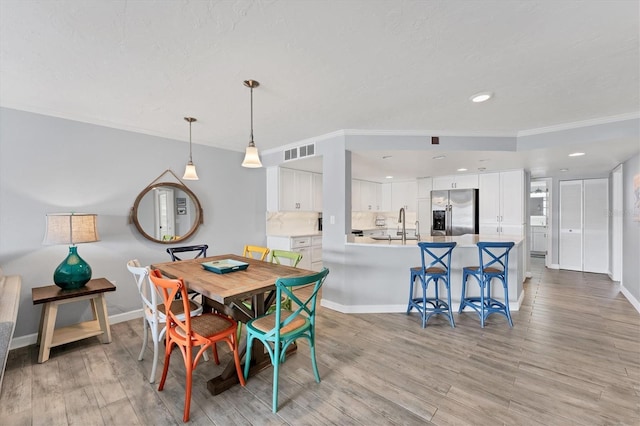 dining area featuring light wood finished floors, baseboards, visible vents, and ornamental molding