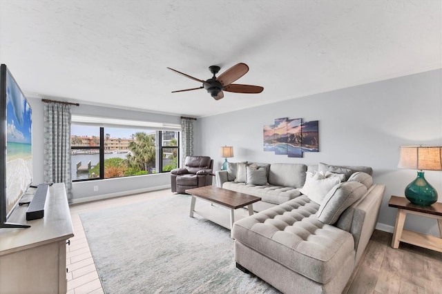 living area with ceiling fan, a textured ceiling, a water view, baseboards, and light wood-type flooring