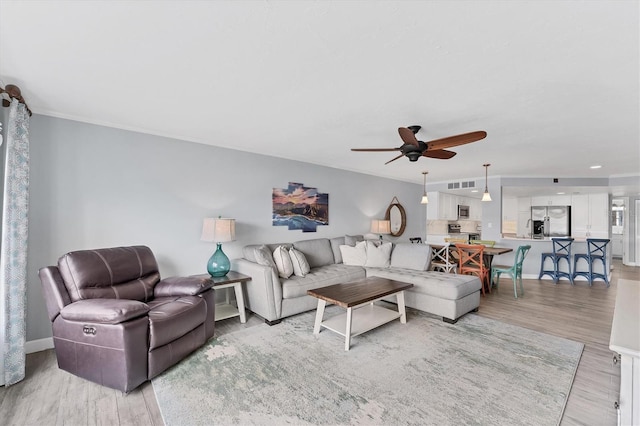 living room featuring ceiling fan, light wood-type flooring, visible vents, and baseboards