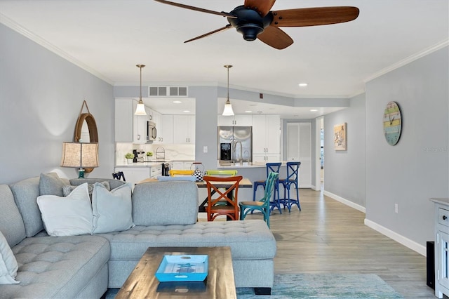 living area featuring ornamental molding, light wood-type flooring, visible vents, and baseboards