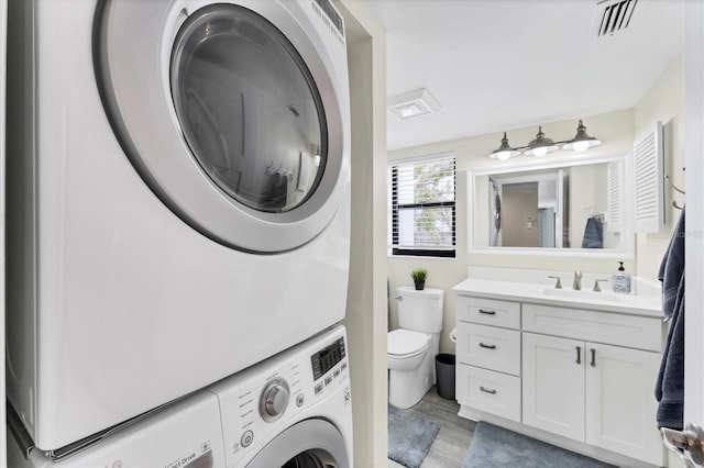 bathroom featuring visible vents, stacked washer / dryer, toilet, wood finished floors, and vanity