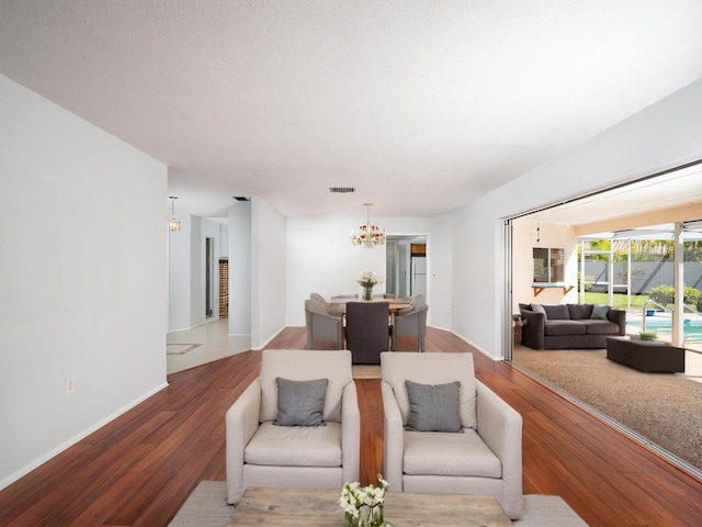 living room with a textured ceiling, visible vents, a notable chandelier, and wood finished floors