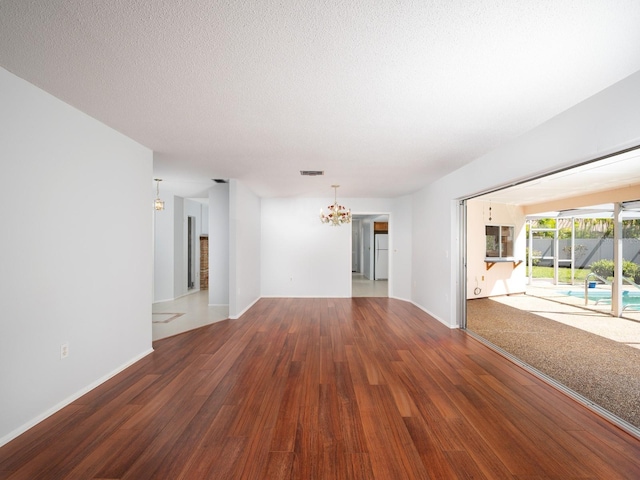 empty room with baseboards, visible vents, wood finished floors, a textured ceiling, and a notable chandelier