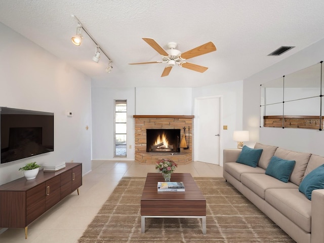 living area with a fireplace, light tile patterned floors, visible vents, a ceiling fan, and a textured ceiling