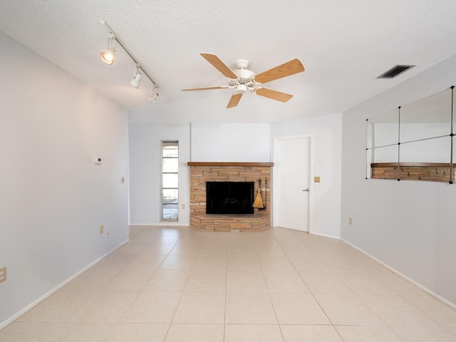 unfurnished living room featuring light tile patterned floors, a ceiling fan, a stone fireplace, a textured ceiling, and baseboards