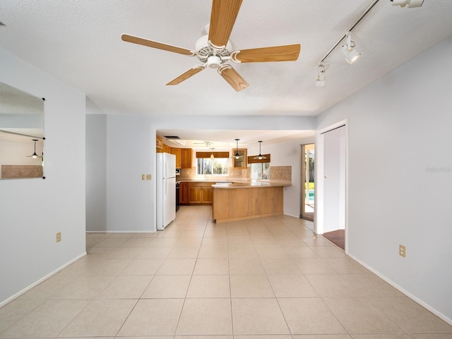 kitchen with a peninsula, open floor plan, light countertops, freestanding refrigerator, and decorative light fixtures