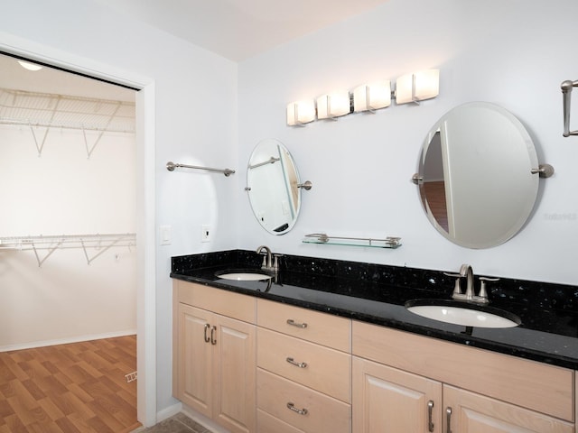 full bathroom with wood finished floors, a sink, baseboards, and double vanity