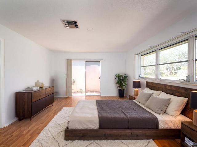 bedroom featuring access to exterior, light wood-type flooring, visible vents, and multiple windows