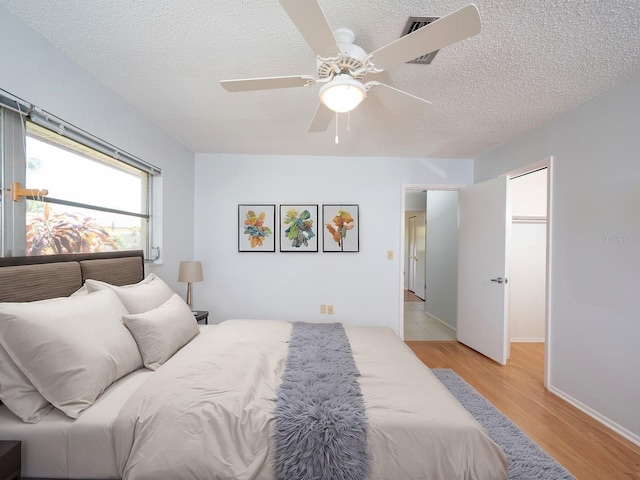 bedroom featuring light wood-type flooring, ceiling fan, baseboards, and a textured ceiling