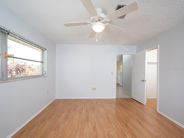 spare room featuring light wood finished floors, baseboards, and a textured ceiling