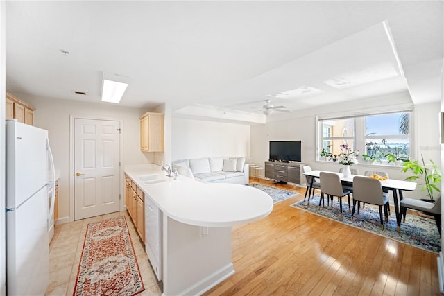 kitchen with light brown cabinetry, freestanding refrigerator, a sink, light wood-type flooring, and a peninsula