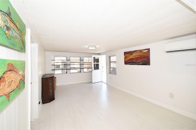 empty room with light wood-style flooring, baseboards, and a wall mounted air conditioner