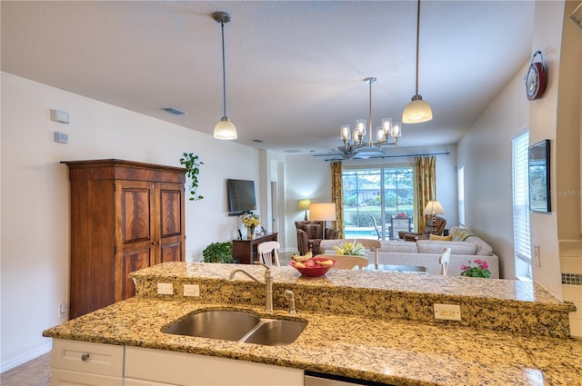 kitchen with light stone counters, open floor plan, white cabinetry, pendant lighting, and a sink