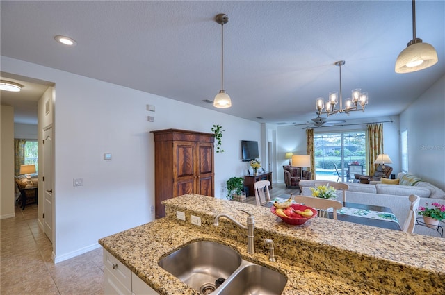 kitchen with light tile patterned floors, open floor plan, decorative light fixtures, light stone countertops, and a sink