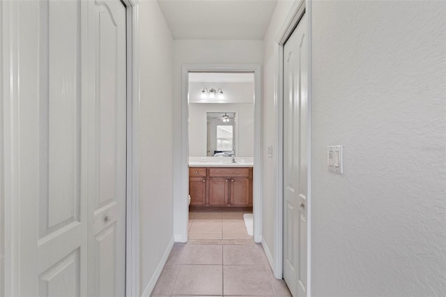 hall featuring light tile patterned floors, a textured wall, a sink, and baseboards