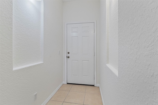 doorway to outside featuring light tile patterned floors, baseboards, and a textured wall