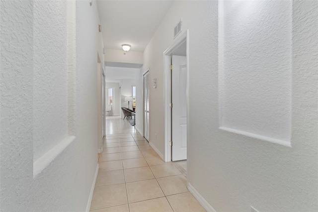 corridor with a textured wall, visible vents, baseboards, and light tile patterned flooring