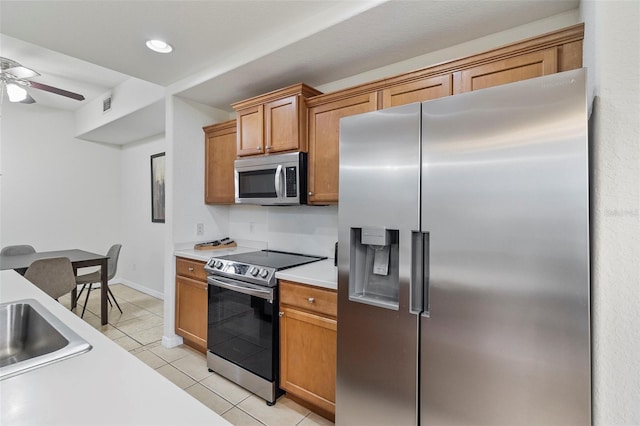 kitchen featuring light countertops, appliances with stainless steel finishes, light tile patterned flooring, and brown cabinets