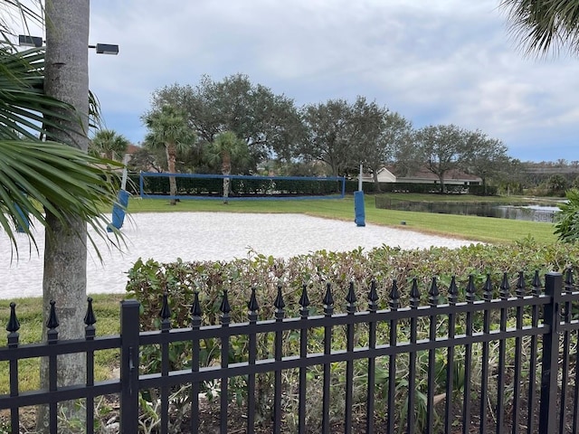 view of property's community featuring a yard, a water view, fence, and volleyball court