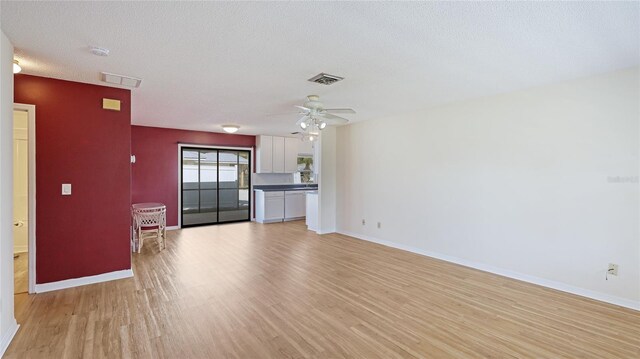 unfurnished living room featuring light wood-style floors, visible vents, a textured ceiling, and baseboards