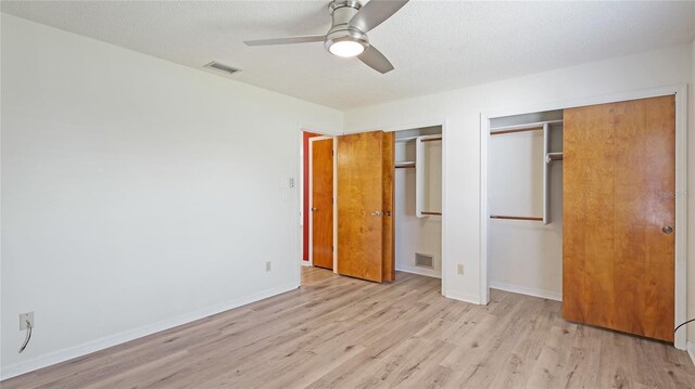 unfurnished bedroom with light wood-type flooring, two closets, visible vents, and baseboards