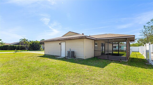 rear view of house featuring a sunroom, central AC, fence, and a lawn