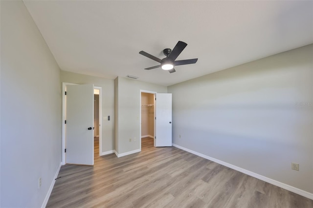 unfurnished bedroom featuring a walk in closet, a closet, light wood-style flooring, a ceiling fan, and baseboards