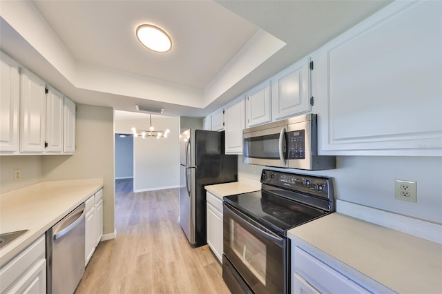 kitchen featuring white cabinets, appliances with stainless steel finishes, a tray ceiling, light countertops, and light wood-type flooring